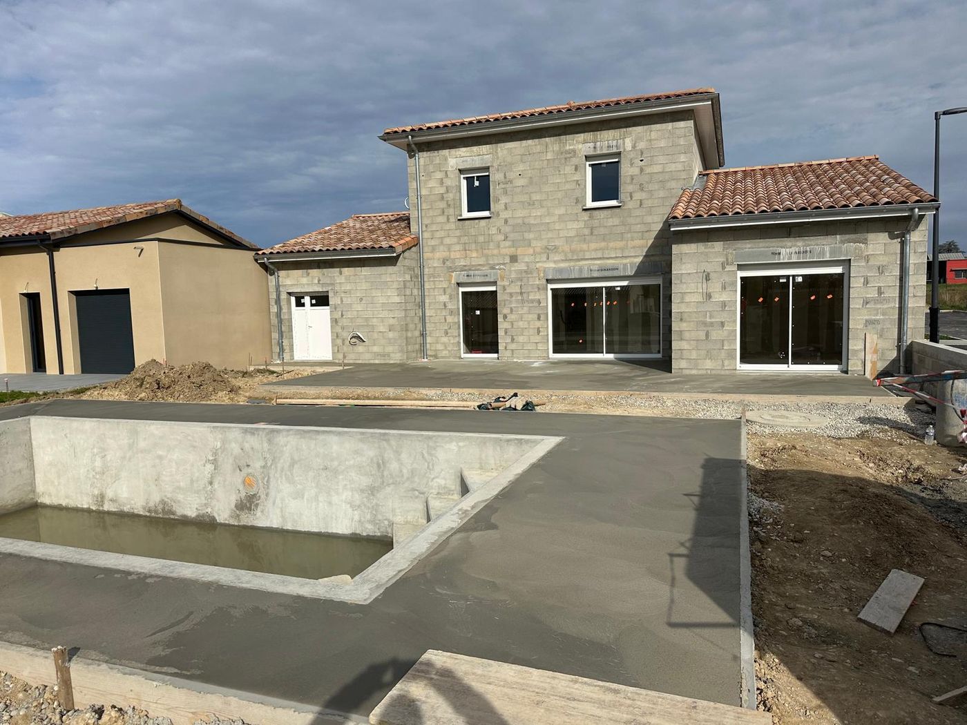 Bassin de piscine en béton et dalle fraîchement coulée devant une maison neuve, réalisation SM BAT